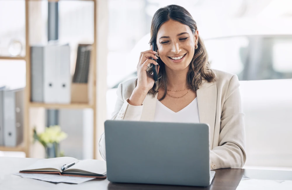 Ein Frau in einem Büro arbeitet an einem Laptop und telefoniert dabei