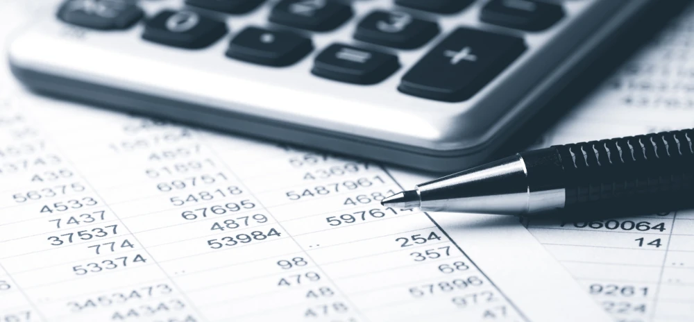 Taschenrechner und Spitze eines Kugelschreibers auf einem Blatt Paiper mit Zahlen